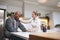 Depressed Mature Man In Dressing Gown Talking With Female Nurse In Kitchen At Home