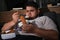 Depressed overweight man eating sweets in room at night