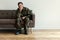 Depressed professional soldier in green uniform sitting alone at home. Copy space on the wall