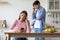 Depressed sad young european woman with smartphone ignores offended angry guy at kitchen interior