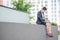 Depressed woman in medical mask sits on parapet outdoors with a box of personal items from the desktop. Unemployed girl