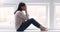 Depressed young mixed race woman sitting on windowsill.