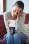 Depressed young woman having headache while drinking coffee on sofa at home