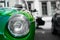 Desatured photo of a close up of the headlight of a green classic sport car, with blurred black and white background