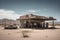A desert gas station , where a few vehicles stand parked in a sea of grit and dust. There\\\'s a fading American flag, but the