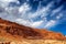 Desert landscape with a towering sandstone rock formation against a blue sky with clouds.