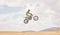 Desert, motorbike cycling and jump for sports, agile driving and off road adventure with mockup space in cloudy sky