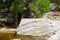 Desert oasis with small pond beside large striped boulder and green plants behind