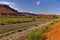 Desert road with green irrigated farmland and huge red mesa in the background