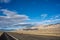 Desert road into valley with brown hill and snowy Sierra Nevada mountains