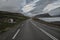 A deserted asphalt road running away into the hills, along the road a waterfall.