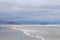 Deserted beach, with beige sand and blue mountain background. Cloudy sky in low light. Small waves in calm sea.