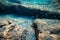 A deserted but fascinating underwater landscape with large rocks, reflections from the setting sun and small shoals of fish in