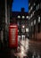 Deserted street at night with traditional royal red British telephone phone box lit up light reflecting on water after rain clears