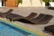 Deserted wicker rattan loungers of an unusual shape on the tiles in front of the pool.