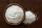 Desiccated coconut in dark wooden bowl isolated on dark brown wood from above. Spilled coconut.