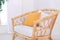Design wicker wooden chair with pillows in stylish light bedroom interior. Rattan armchair by the white wall in the living room.