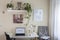 desk with laptop and chair in front, shelves with plants and on the right a window with a white curtain, home office