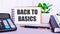 On the desktop are a calculator, diaries, a potted plant, a pen and a notebook with the text BACK TO BASICS. Business concept.