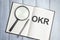 Desktop magnifier, reports, pen and notebook with text OKR Objective Key Results