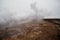 Desolate landscape of Iceland volcanic brown soil with steamy geyser mist