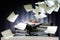 Desperate woman sinks behind stacks of ring binders on an office desk and lots of papers are flying down, concept of excessive