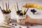 Dessert in glass with granola, chocolate, banana and blackberries decorated with sticks Pocky in female hand on gray background,