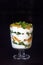 Dessert layered in a transparent glass, yogurt, orange, kiwi, nuts on a dark background. The concept of healthy, proper and simple