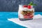 Dessert with strawberry, granola and cottage cheese in glass on blue background with copy space