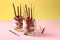 Dessert in two glasses with chocolate granola, banana and raspberry, decorated with sticks Pocky on yellow and pink background