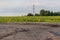 The destroyed part and the crumbling piece of asphalt with electric pole on a field with sunflowers out of focus of the