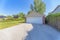 Detached garage exterior with white sectional door and concrete driveway near the wall of plants