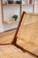 Detail of backrest of modern wicker chair standing in a living room with shelves with decorations and plants.