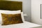 Detail of a bedroom with ocher green velvet upholstered headboard and matching cushions