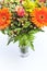 Detail of a bouquet of orange, yellow and red flowers in a vase.