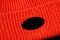 Detail of a bright, knitted orange hat with a blank, black tag, mockup, closeup.