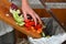 Detail of a female hand disposing of organic waste in a proper bin with kitchen in the background