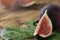 Detail of freshly cut fig with green leaf on a wooden table. There are raw figs in the background