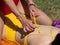 Detail of a girl`s hands unbuttoning a knot in another girl`s bathing suit lying on the grass to massage her