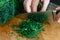 Detail of hands chopping up a bunch of dill on wood chopping boa