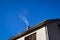 Detail of house,smoke raising from a chimney in winter against blue clear sky, low angle copy space