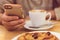 Detail image of unrecognisable man drinking coffee and holding smart phone while having breakfast in restaurant.