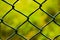 Detail of intertwined metal fence with green fence background