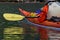 Detail of kayaker in orange jacket and orange kayak with her yellow paddle blade reflected in the water