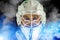 Detail of a male face in a white goalie hockey mask and  blue and white smoke.