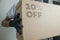 Detail of man with black gloves holding a cardboard box with 10% discount for delivering products on gray background.