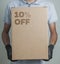 Detail of man with black gloves holding a cardboard box with 10% discount for delivering products on gray background.