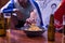 Detail of a man`s hand grabbing a french fry from a bowl with beers next to it, at the living room table of two friends watching