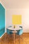 Detail of modern table and chairs with parquet floor, yellow frame and turquoise wall