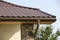 Detail of new modern house cottage corner with stucco walls decorated with natural stones, brown shingled roof and rain gutter pip